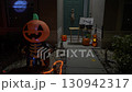 Spooky Halloween porch at night with a glowing inflatable pumpkin skeleton and carved jack-o-lanterns. The front door and window show pumpkins, skulls, bones, and festive lights for trick-or-treat. 130942317
