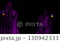 Close-up Halloween yard decoration shows a hooded ghost holding a lantern in purple light at night. Spooky outdoor scene features a skull face, draped fabric, and a glowing lamp against a dark 130942333