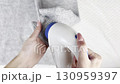 A woman uses a fabric shaver to remove pilling from her warm autumn winter sweater. Clothes care, wardrobe preparation for cold season, lint remover cleaning knitwear and cozy wool garments 130959397