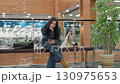 Remote worker seated on bench inside spacious mall browses phone calmly, surrounded by shopping bags, glass railing, artificial tree, and glowing ceiling lights reflecting on polished floor 130975653