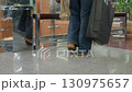Low angle view of shopper in brown shoes walking toward bench inside shopping mall, carrying black and brown shopping bags, preparing to sit in relaxed posture beside indoor plant and glass railing 130975657