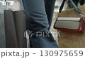 Close up of shopper walking through modern mall carrying black and brown shopping bags with visible handbag on paper bag, heading toward bench as other shoppers blur in background 130975659