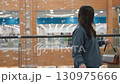 Female shopper in casual outfit stands near glass railing of modern mall, gazing at colorful retail store below while waiting for friend after shopping, surrounded by soft lights and flying decor 130975666