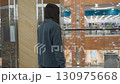 Young lady in loose blue outfit seen from back inside modern shopping mall pauses near bench after shopping, prepares to sit with shopping bag as background reveals vibrant retail clothing section 130975668