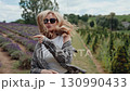 Blonde woman radiating joy, wearing sunglasses and checkered shirt, dancing freely among lavender blooms, embodying carefree summer spirit and pure happiness. Blonde dancing amid lavender field 130990433