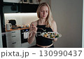 Portrait of adult athletic woman enjoying nutrient dense salad in sleek contemporary kitchen, highlighting mindful eating and wellness through deliberate. Woman savoring colorful packed salad 130990437