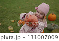 Little girl smiles while holding a pumpkin in a field full of autumn harvest 131007009