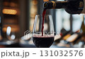 Pouring a fine Red Wine into a pristine Glass while Grapes are beautifully arranged on a Rustic Wooden Table 131032576