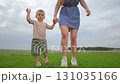 Mother and boy walking hand in hand across green grass. Outdoor bonding builds love and support. Child enjoys walking beside mother. Holding hands brings comfort. Walking together shows love and trust 131035166
