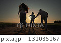Father holds bicycle while boy pedals forward. Outdoor sunset shines behind family. Mother follows running. Parents help child. Boy rides bicycle slowly. Outdoor moment connects father, child mother. 131035167