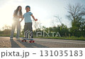 Happy boy enjoys skateboard ride with mother. Ride builds fun connection between child and mother. Outdoor skateboard session brings happy moment. Boy laughs during skateboard ride in outdoor space. 131035183