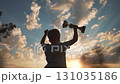 Boy celebrates success lifting trophy in glowing sunset. Trophy in hands of kid reflects sky light. Silhouette of boy shows winner joy. Kid wins trophy in sunset success moment. Winner joy under sky. 131035186