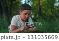 Young student, girl explorer, leans over rock with magnifier. Child explores nature, explores discovery, discovery becomes learning, learning becomes research, research becomes connection with forest. 131035669