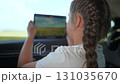 Schoolgirl traveler girl sits in moving car watching screen. Viewer girl, student viewer, tourist viewer rides calmly. Girl traveler, teen passenger, child viewer looking outside during trip. 131035670