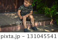 the child touches a scab on his knee with his finger while sitting on the porch on a hot summer day the camera slowly moves closer he is wearing a t shirt and shorts 131045541