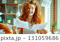 Portrait of a happy young woman holding a document with great news and papers flying in the air. 131059686