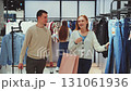 Young couple enjoying shopping in clothing store, woman holding bag and browsing clothes while man walks beside her with purchases 131061936