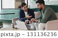Two colleagues collaborate in office, reviewing documents using laptop 131136236