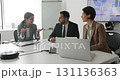 Three business professionals engaged in discussion during briefing in boardroom 131136363