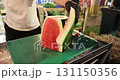 Gloved person cuts the rind off a watermelon at the evening street food festival 131150356
