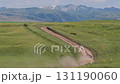 Suv car driving on dirt road in green meadow with snowy mountains background 131190060