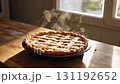 Steaming golden-brown lattice pie on a rustic wooden table by a sunlit window 131192652