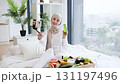 Muslim woman in hijab filming skincare blog on smartphone at home, promoting daily beauty routines with green moisturizing lotion, healthy fruits, natural light. 131197496