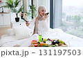 Young Muslim woman recording video for blog about self-care routine with natural ingredients. Depicts healthy lifestyle and creative content creation in bright modern home environment with products. 131197503
