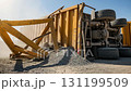 A yellow construction truck lies on its side at a construction site, surrounded by spilled gravel and twisted metal beams. Dust particles float in the bright sunlight, highlighting the scene. 131199509