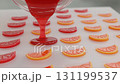 Liquid candy flows smoothly into silicone molds shaped like fruit slices, showcasing bright reds and oranges under the factory lights, creating a colorful confectionery treat. 131199537