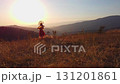 Drone flies over young woman in autumn outfit on meadow in mountains on sunset background 131201861