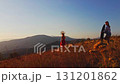 Drone flies over film crew and young woman in autumn outfit on meadow in mountains on sunset background 131201862