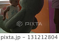 A baby girl with short blond hair in a blue suit lifts a huge blue teddy bear in her arms and looks at it with delight, smiles, and watches as her mother takes it and holds it in the air 131212804