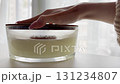 Woman hand opening wooden lid of large scented candle in glass jar, cozy home interior, warm autumn mood, hygge style 131234807