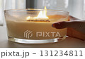 Woman hand moving large scented candle in glass jar burning in cozy autumn home interior, warm hygge aromatherapy mood 131234811