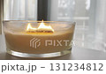 Large scented candle in glass jar burning in cozy autumn home interior, warm hygge atmosphere, aromatherapy 131234812