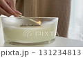 Lighting scented candle in glass jar with match, woman hand close up, cozy home interior and autumn hygge mood 131234813