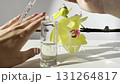 Woman hand applying glass cosmetic pipette with transparent serum from bottle on light background with orchid and natural sunlight. Skincare beauty product 131264817