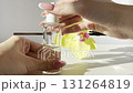 Woman hand holding glass cosmetic pipette with clear facial serum and bottle on light background with orchid and natural sunlight. Skincare beauty product 131264819