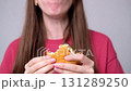 Young woman in a red T-shirt eating a hamburger in a studio against a white wall 131289250