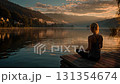 Young woman practicing yoga at sunrise on a wooden pier in a mountain lake 131354674
