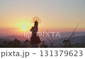 Young female model in designer headdress made of spikelets and dress made of flowers and grass on the background of sunset in the mountains. 131379623