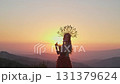 Young female model in designer headdress made of spikelets and dress made of flowers and grass on the background of sunset in the mountains. 131379624