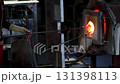 Close-up glassblowing process tube tool with molten glass shaped inside refractory furnace in industrial craft workshop. Handmade blowing glassware design production manufacture Europe 131398113