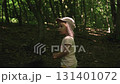 A baby girl in a pink dress and a Panama hat walks along a path in the forest among tall green trees, loses sight of her mother looks around confusion fear, searching her eyes, lost in the forest 131401072