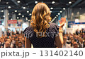Young female speaker in crowded business audience gives speech. Woman is on commercial conference session. Lecture in exposition hall 131402140