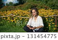 Social network communication, woman wearing white shirt sitting near yellow flowers field and typing on a smartphone, surf internet, mature-age student. 131454775