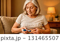 Senior woman with gray hair is administering medication using a pen injector on her abdomen while seated comfortably in a cozy living room, showcasing self-care and health management 131465507