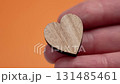 Wooden heart symbol on a hand palm close up. Orange background. Valentine day and love concept 131485461