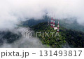 A mountain with a tower on top and a foggy sky. The tower is red and white 131493817
